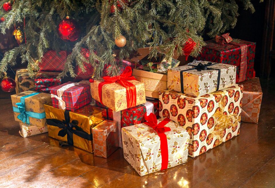 Wrapped gifts with colourful ribbons placed under a decorated Christmas tree adorned with red baubles and festive ornaments.